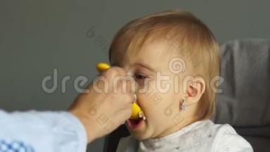 漂亮的蓝眼睛宝宝坐在高椅上，尽职地吃着捣碎的蔬菜，张开嘴。 妈妈给孩子喂奶